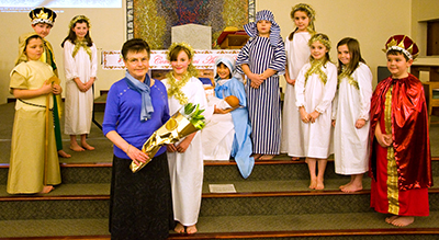 Gladys Galloway is presented with flowers by the Angel Gabriel as a thankyou for making the costumes.